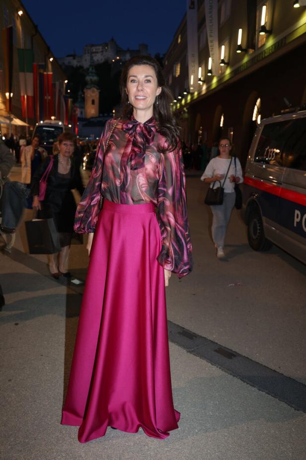 Eine Frau in einem langen, pinkfarbenen Rock und einer gemusterten Bluse in einer Stadtstraße.