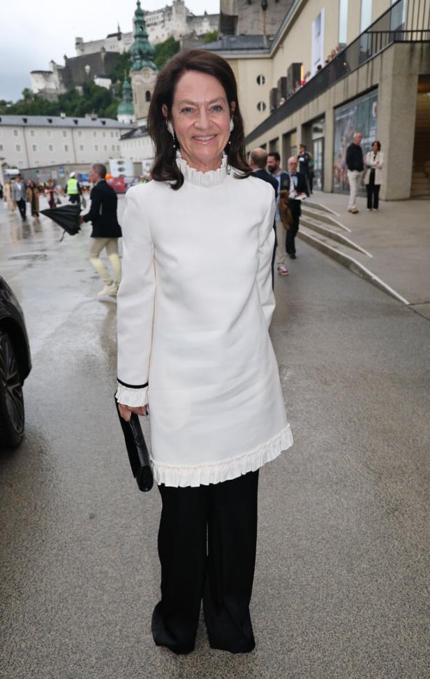 Eine Frau in einem weißen Kleid und schwarzen Hosen vor der Festung Hohensalzburg.