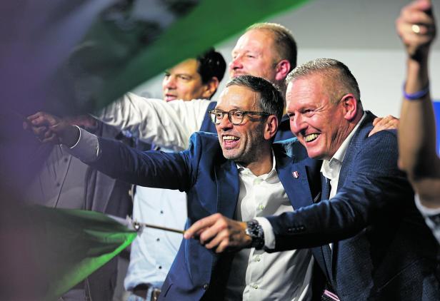 Herbert Kickl und Mario Kunasek stehen zusammen auf einer Bühne, im Hintergrund andere Männer, beide haben eine Steiermark-Fahne in der Hand die sie schwenken 