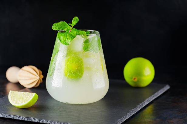 Mojito-Cocktail mit Limette, Minze und einem hölzernen Entsafter auf einem dunklen Hintergrund.
