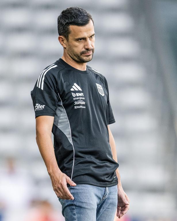 Ein Mann in Sportkleidung und Jeans steht auf dem Rasen.