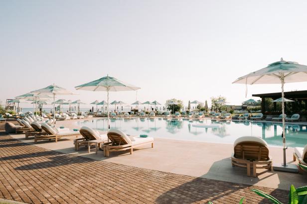 Liegestühle und Sonnenschirme stehen an einem Pool im Armani Mare am 91 Athens Riviera.