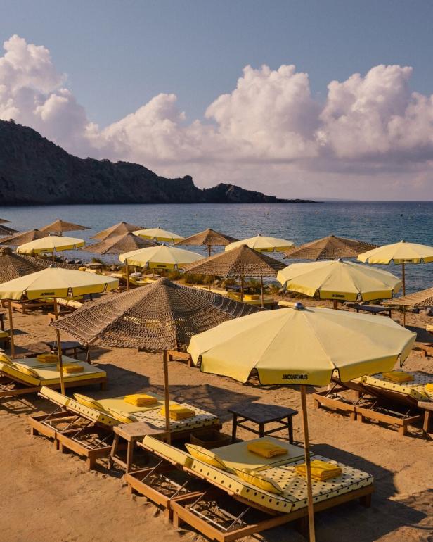 Gelbe Sonnenschirme und Liegen am Strand vor einer felsigen Küste.