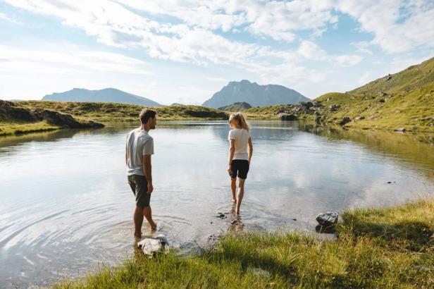  Zwei Personen stehen in einem See, im Hintergrund sind majestätische Berge zu sehen..