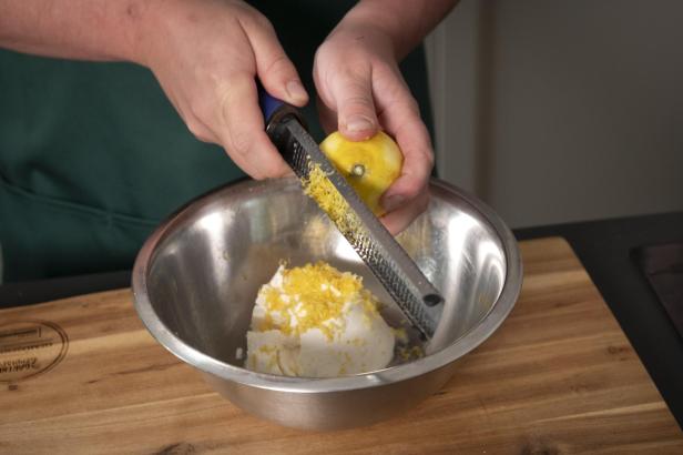 Eine Person reibt Zitronenschale in eine Schüssel mit Ricotta-Creme.