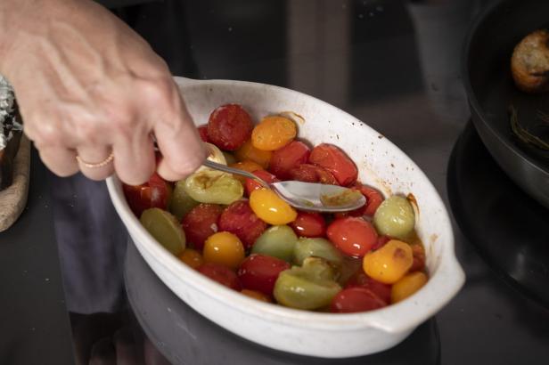 Eine Person zerdrückt geröstete Tomaten in einer Auflaufform.