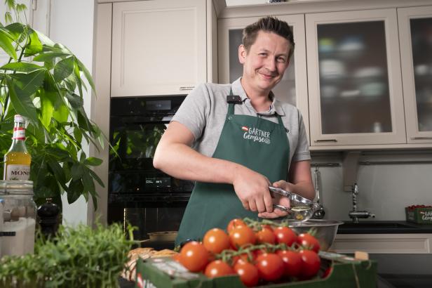 Ein Mann steht in einer Küche vor Tomaten.