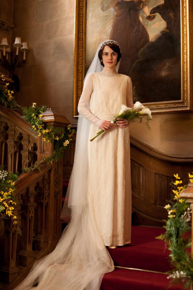Eine Frau im Brautkleid mit Schleier und Blumenstrauß steht auf einer Treppe.