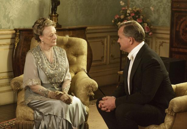 Violet Crawley, Dowager Countess of Grantham, sitzt in einem Sessel und spricht mit einem Mann.