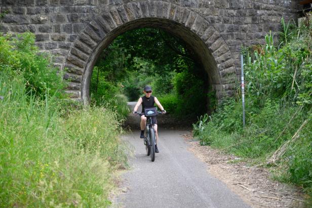 Radfahrerin auf der Parenzana Strecke fährt unter einem Viadukt durch.
