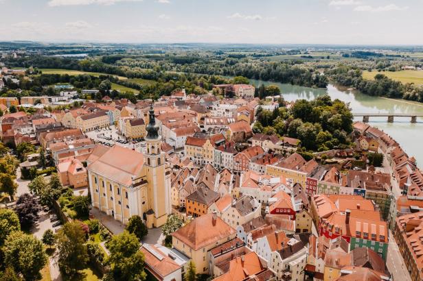 Luftaufnahme von einer Stadt mit rotem Ziegeldach und einer gelben Kirche am Fluss.