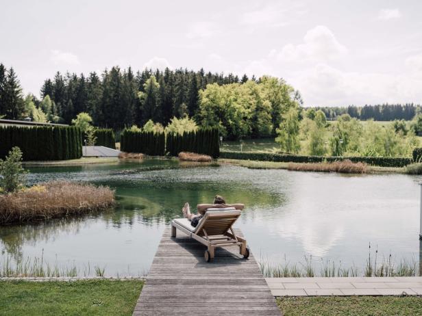 Ein Mann liegt auf einer Liege auf einem Steg - und sieht auf den großen Schwimmteich hinaus.