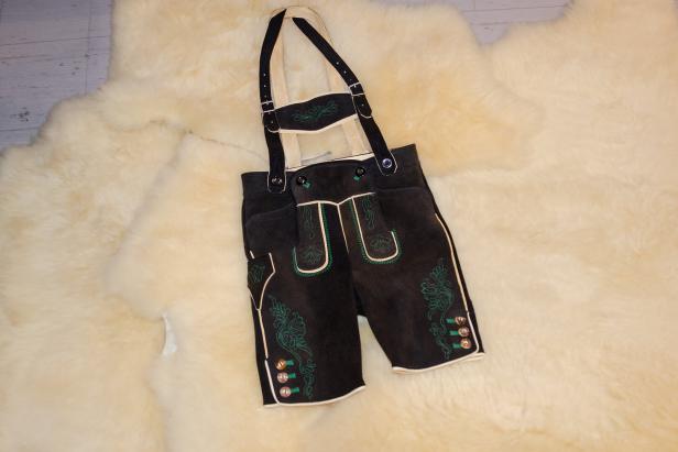 Eine traditionelle, kurze Lederhose mit Hosenträgern liegt auf einem Schaffell.