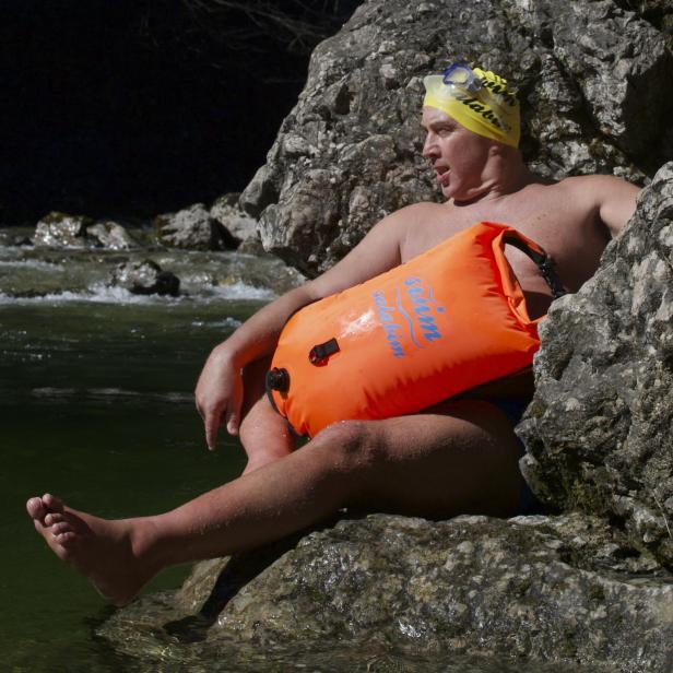 Hansjörg Ransmayr sitzt mit Schwimmboje an einem Flussufer.