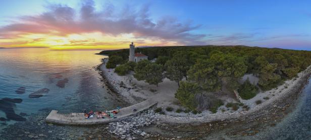 Menschen genießen den Sonnenuntergang auf der Insel Vir mit Blick auf einen Leuchtturm.