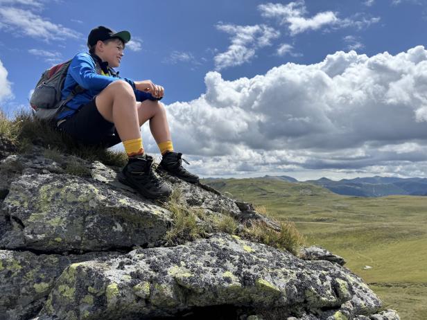Kind sitzt auf einem Felsen und schaut in die Landschaft.