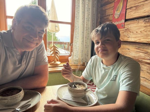 Vater und Kind essen Fritattensuppe auf einer Berghütte.