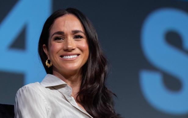 Meghan Markle lächelt vor einem blauen Hintergrund.
