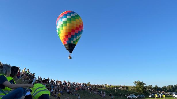 Ein Heißluftballon in Regenbogenfarben fährt über den mit Zuschauern belegten Hang in Wieselburg.