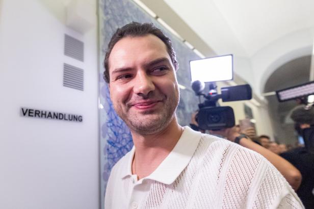 Jimi Blue Ochsenknecht lächelt vor einer Wand mit der Aufschrift "Verhandlung", umringt von Kameras.