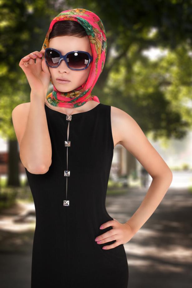 Eine junge Frau im schwarzen Kleid trägt ein Tuch im 1950er-Stil.