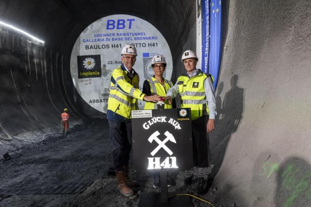 Drei Personen mit Warnwesten stehen vor der zu sprengenden Wand im Brennerbasistunnel.