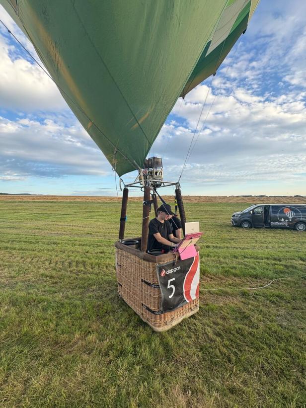 Zwei Personen im Korb eines Heißluftballons auf einem Feld.