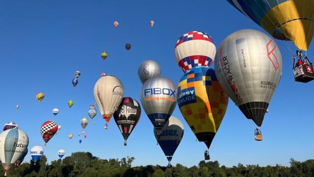 Viele bunte Heißluftballons steigen in den blauen Himmel auf.
