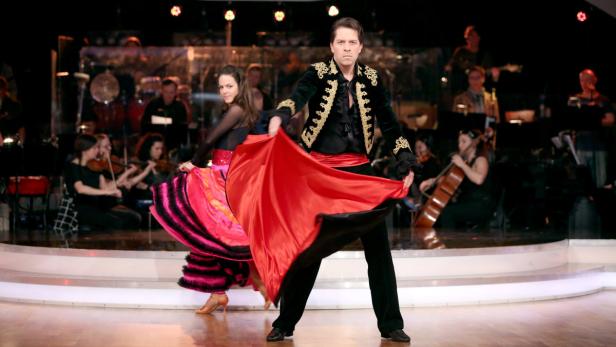 Ein Mann und eine Frau tanzen Flamenco vor einem Orchester.