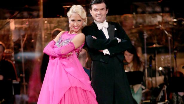 Ein Mann im Smoking und eine Frau im pinkfarbenen Ballkleid posieren lächelnd.