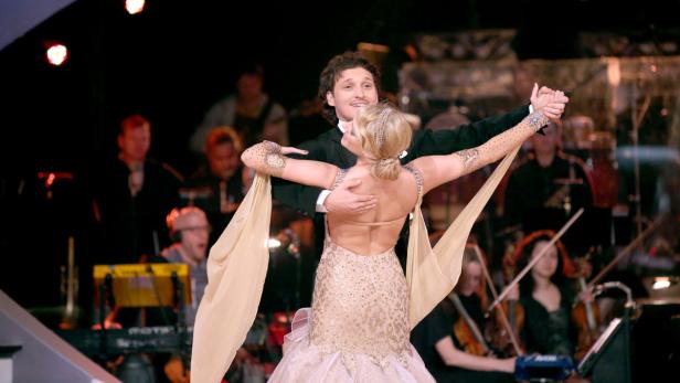 Ein Tanzpaar führt vor einem Orchester eine elegante Tanzdarbietung auf.