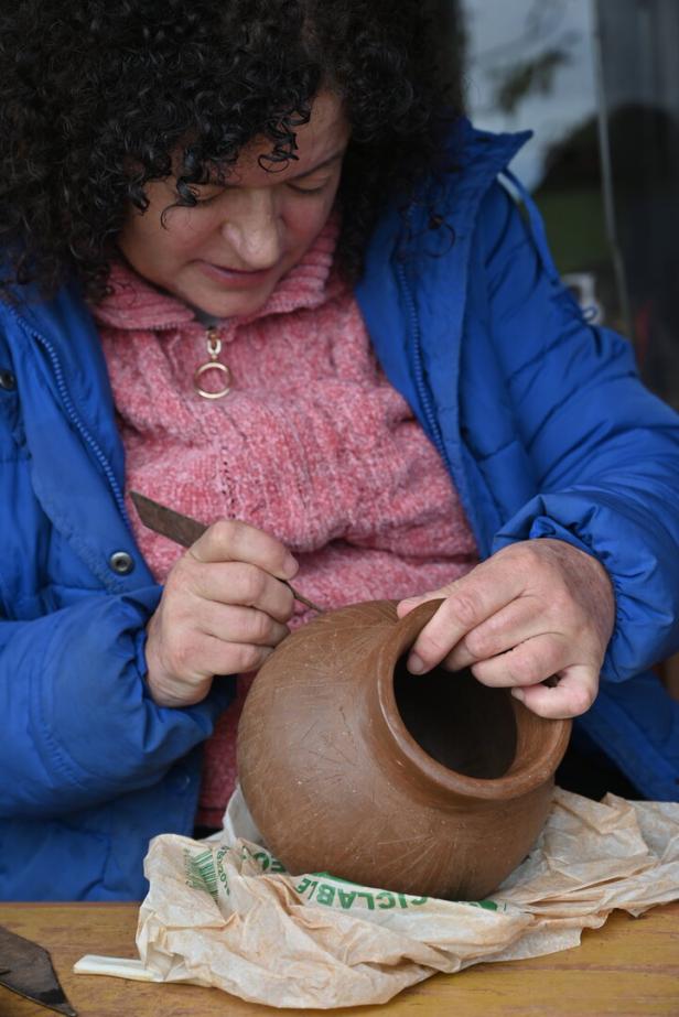 Eine Frau verziert eine braune Tonvase mit einem Werkzeug.