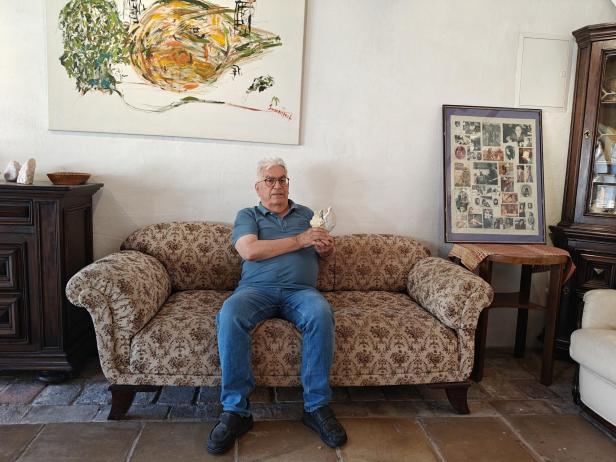 Manfred Pawlik sitzt auf einem Sofa und hält eine Skulptur.