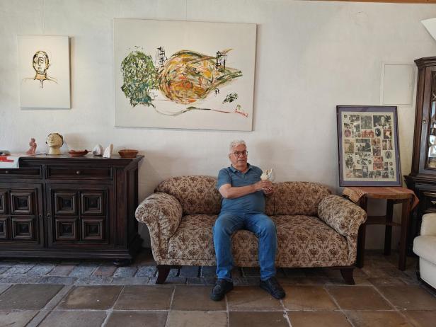 Manfred Pawlik sitzt auf einem Sofa in einem Raum mit Kunstwerken.