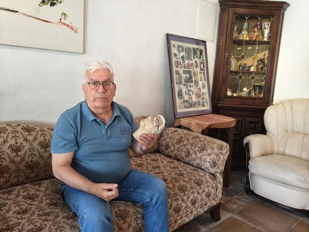 Manfred Pawlik sitzt auf einem Sofa und hält eine Maske in der Hand.