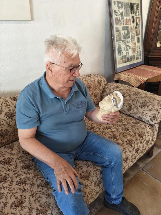 Manfred Pawlik betrachtet eine Kopf-Skulptur auf einem Sofa sitzend.