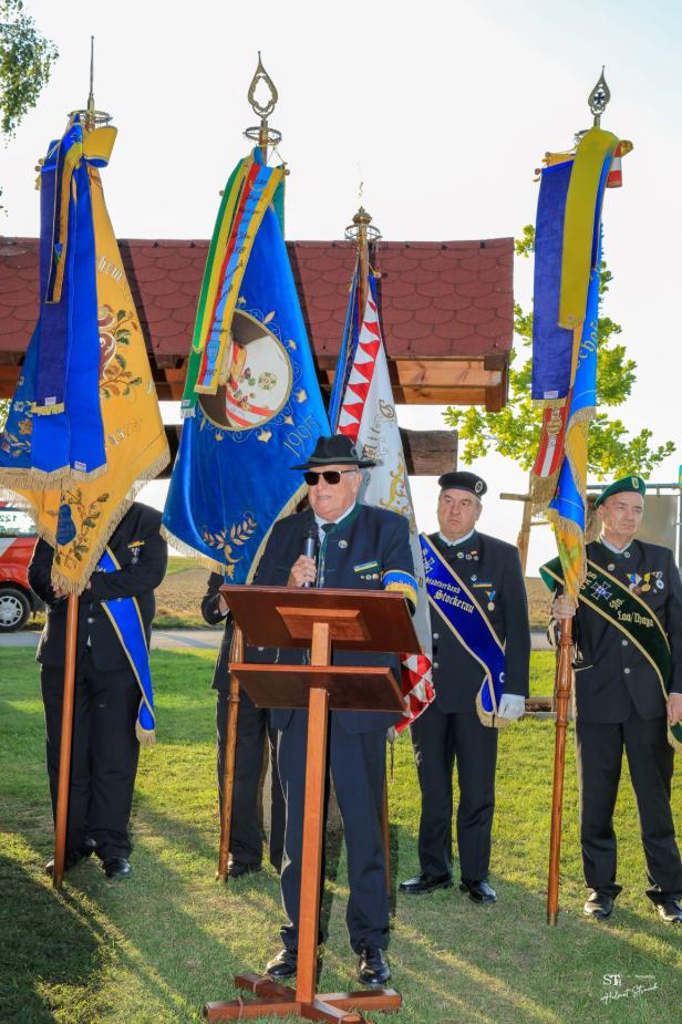Ein Mann hält eine Rede vor mehreren Fahnen bei der „Friedens- und Freiheitsfeier Großharras“.
