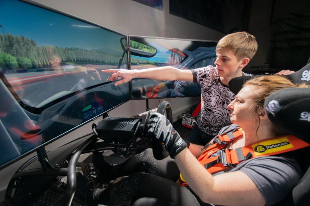 Eine Frau fährt einen Rennsimulator, ein junger Mann zeigt auf den Bildschirm.