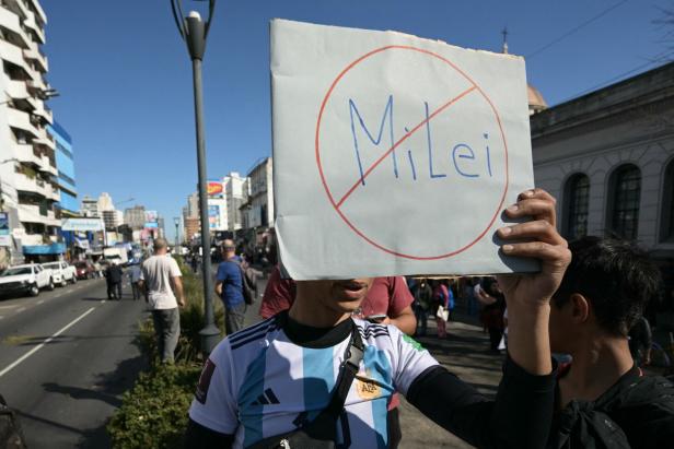 Mann auf Straße hält Schild mit dem durchgestrichenen Namen Milei hoch.