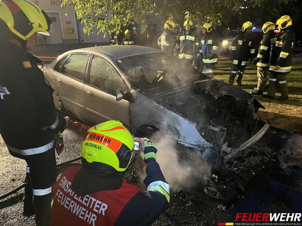 Ausgebranntes Auto mit Feuerwehrmännern