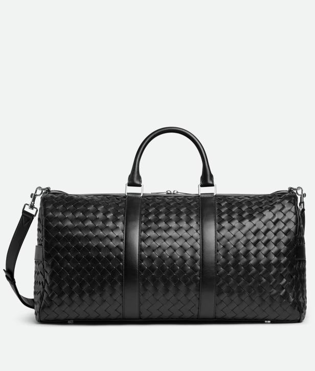 Eine schwarze Reisetasche aus geflochtenem Leder mit Tragegriff und Schultergurt.