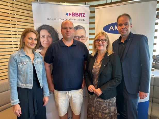 Eine Gruppe von vier Personen posiert vor Bannern von BBRZ und AMS.