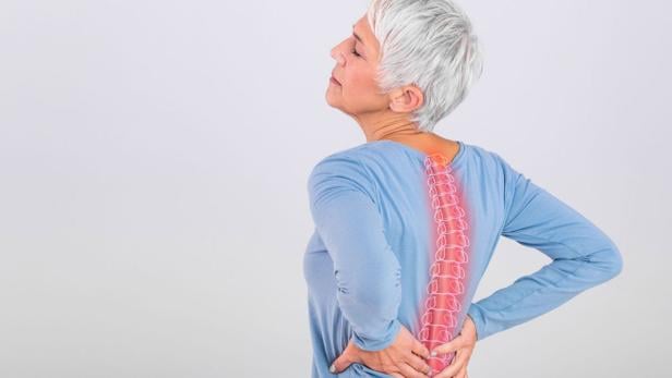 Krafttraining stärkt Muskeln und Knochen und schützt somit vor Osteoporose. Eine alte Frau mit grauen Haaren hält sich ihren Rücken.