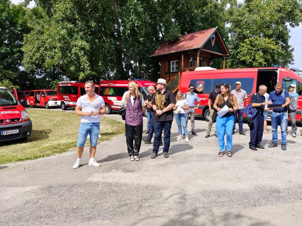 Eine Gruppe von Menschen steht vor roten Feuerwehrfahrzeugen in Marchegg, Marchfeld.