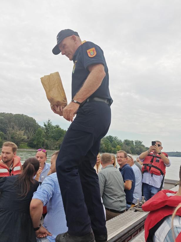 Ein Mann in Uniform steht auf einem Boot und hält eine Papiertüte.