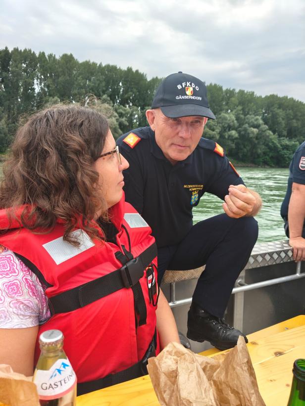 Eine Frau mit Rettungsweste spricht mit einem Feuerwehrmann auf einem Boot.