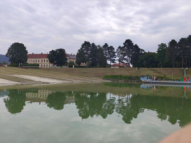 Blick auf den Marchfeldkanal mit einem Gebäude und Bäumen im Hintergrund.