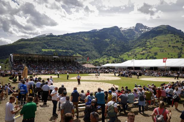 Ein Schwingfest vor einer Bergkulisse mit Zuschauern auf Tribünen.