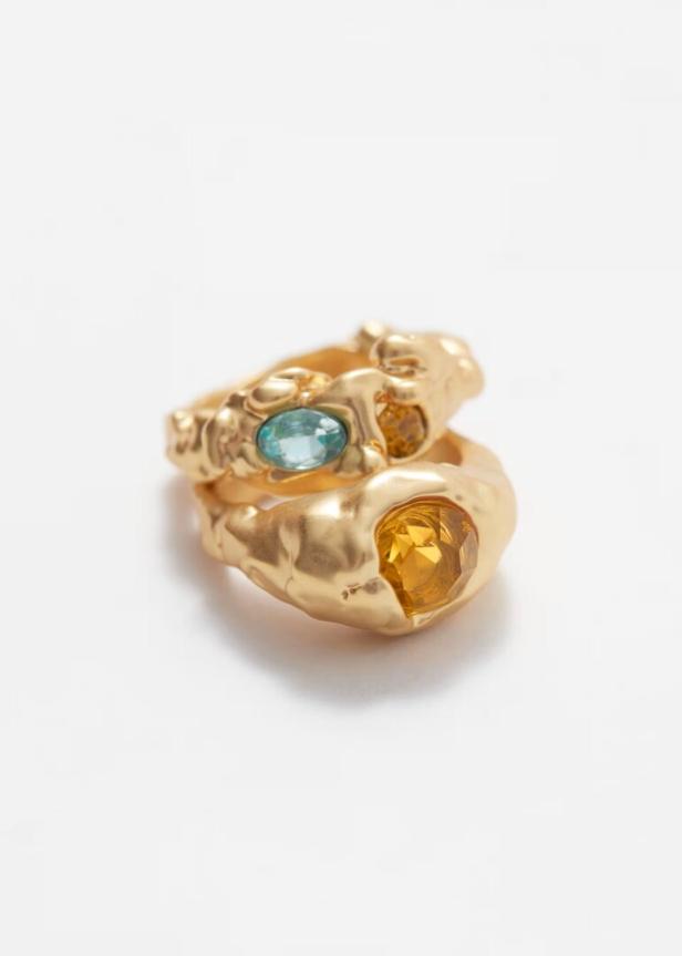 Zwei goldene Ringe mit blauen und gelben Schmucksteinen liegen übereinander.