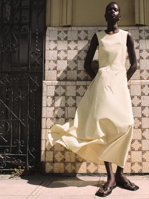 Eine Frau in einem hellgelben Kleid posiert vor einer verzierten Wand.